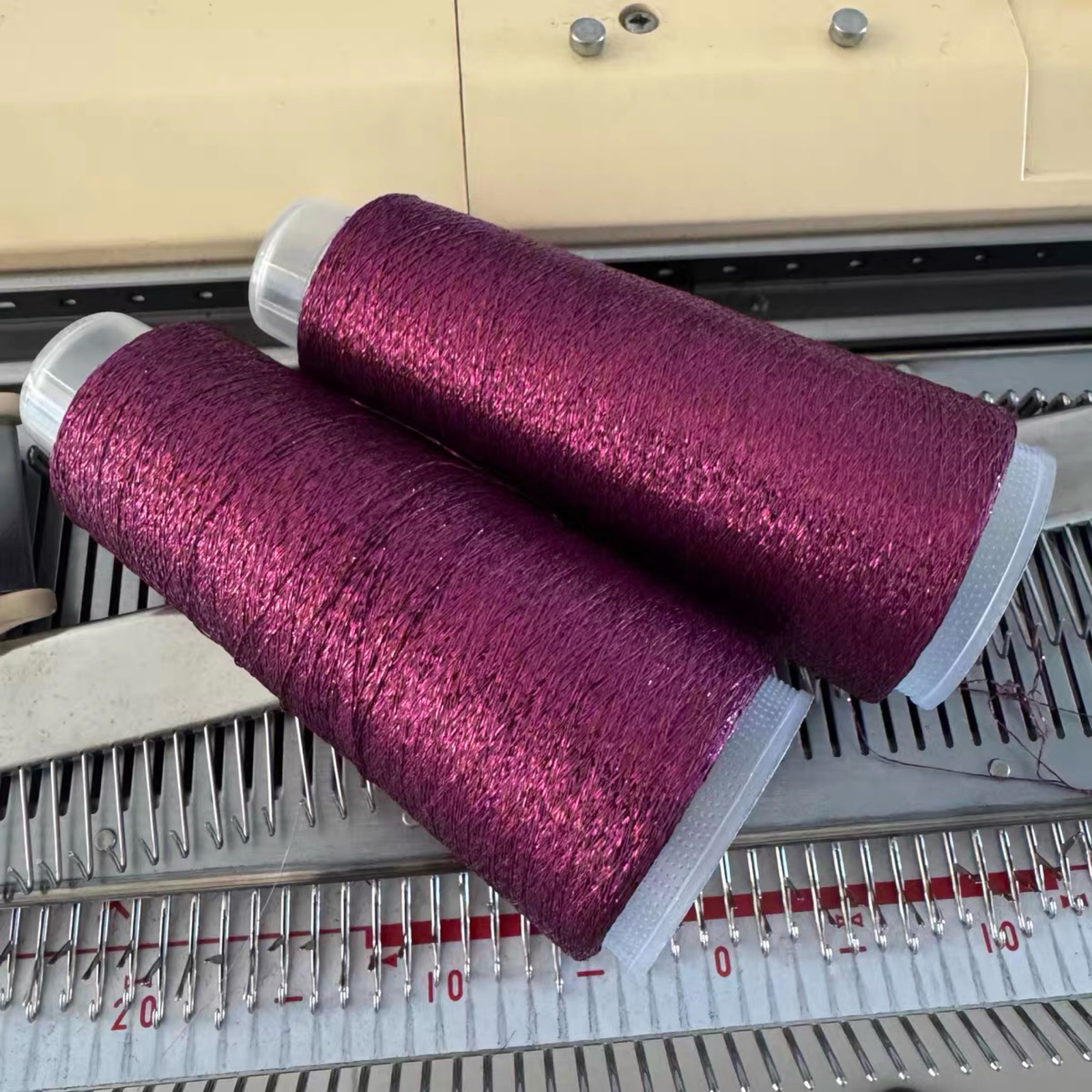 Two cones of purple-red yarn on the knitting machine